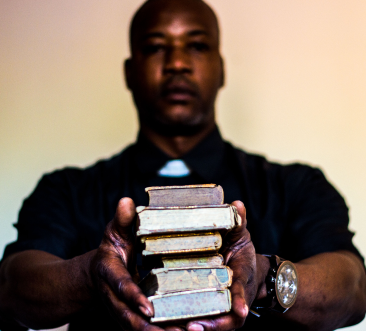 Photographie de l'ariste Don Bakano qui pose avec des livres dans ses mains.